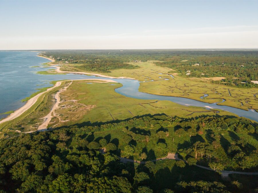 Drone photograph of the Cape Cod coastline with marshes, dunes, and a quiet beach at sunset.