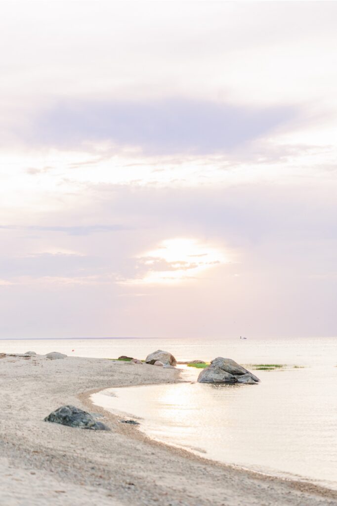 Peaceful Cape Cod beach shoreline with glowing sunset light over the water.
