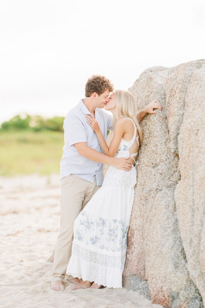 Couple sharing a kiss beside a large granite boulder on a Cape Cod beach.