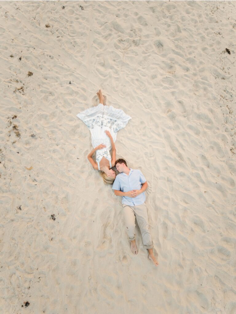 Drone view of a couple lying together in the sand during Cape Cod beach engagement photos.