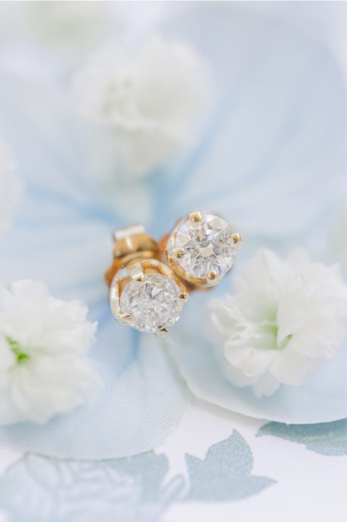 Diamond stud earrings styled with white flowers and pale blue ribbon.