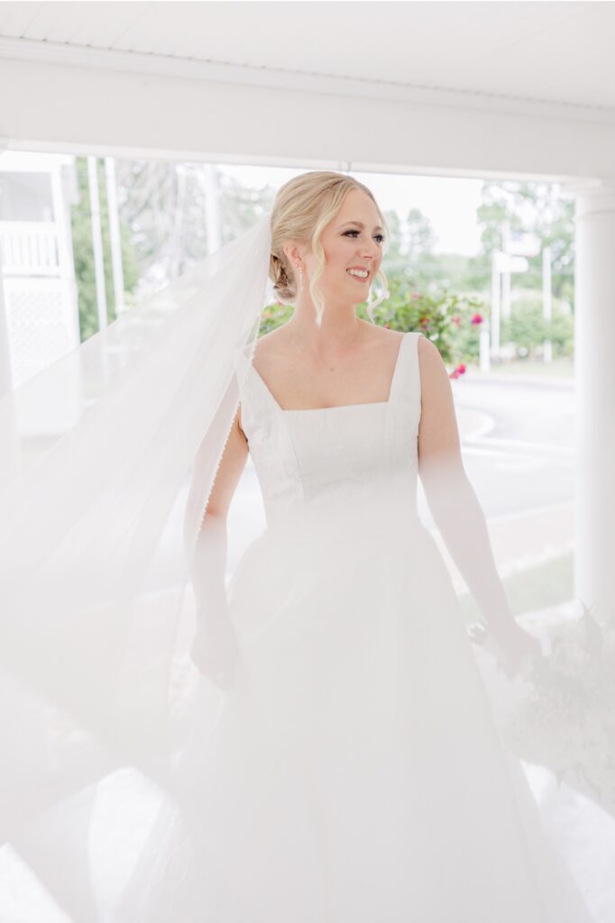 Smiling bride with her veil flowing behind her on the Publick House porch.