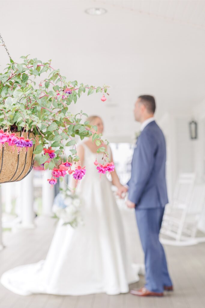 Colorful hanging flowers frame a bride and groom holding hands on the Publick House porch.
