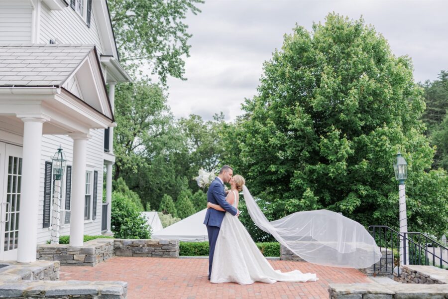 Bride and groom kiss outside the Publick House Historic Inn with her veil flowing behind them.