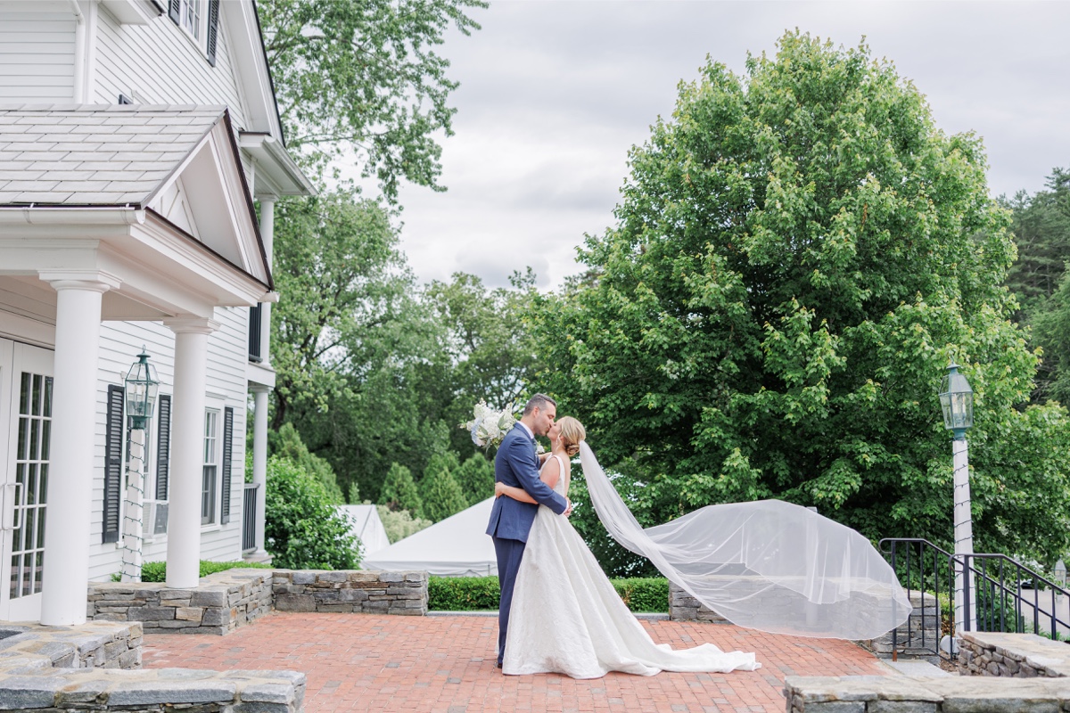 Bride and groom kiss outside the Publick House Historic Inn with her veil flowing behind them.