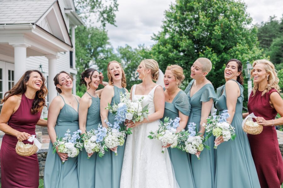 Bride laughs with her bridesmaids in sage green dresses outside the Publick House.