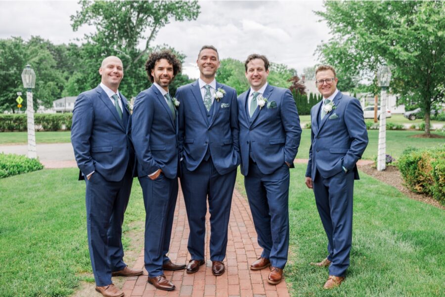 Groom and groomsmen in navy suits pose on the Publick House lawn.