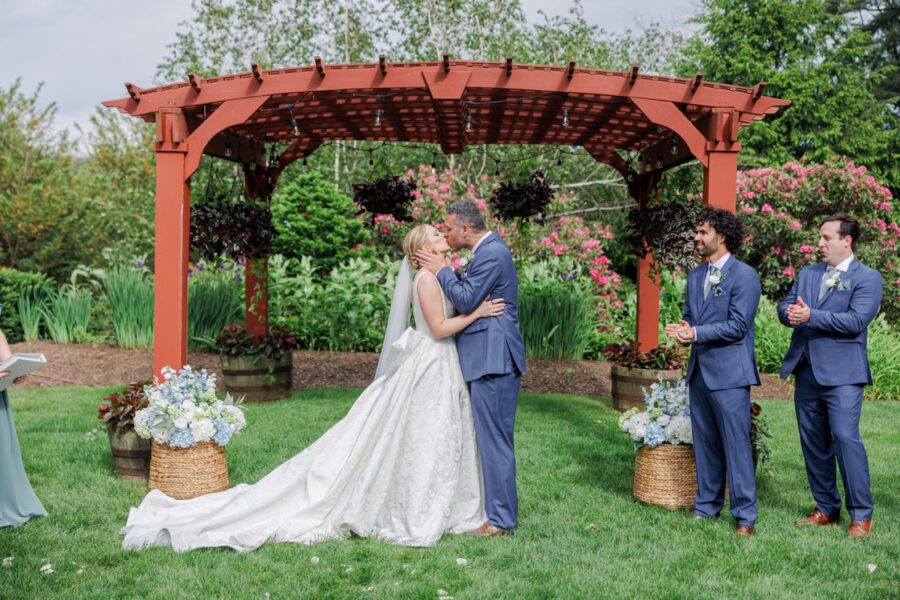 Newlyweds share their first kiss beneath the garden arbor at their Publick House wedding.