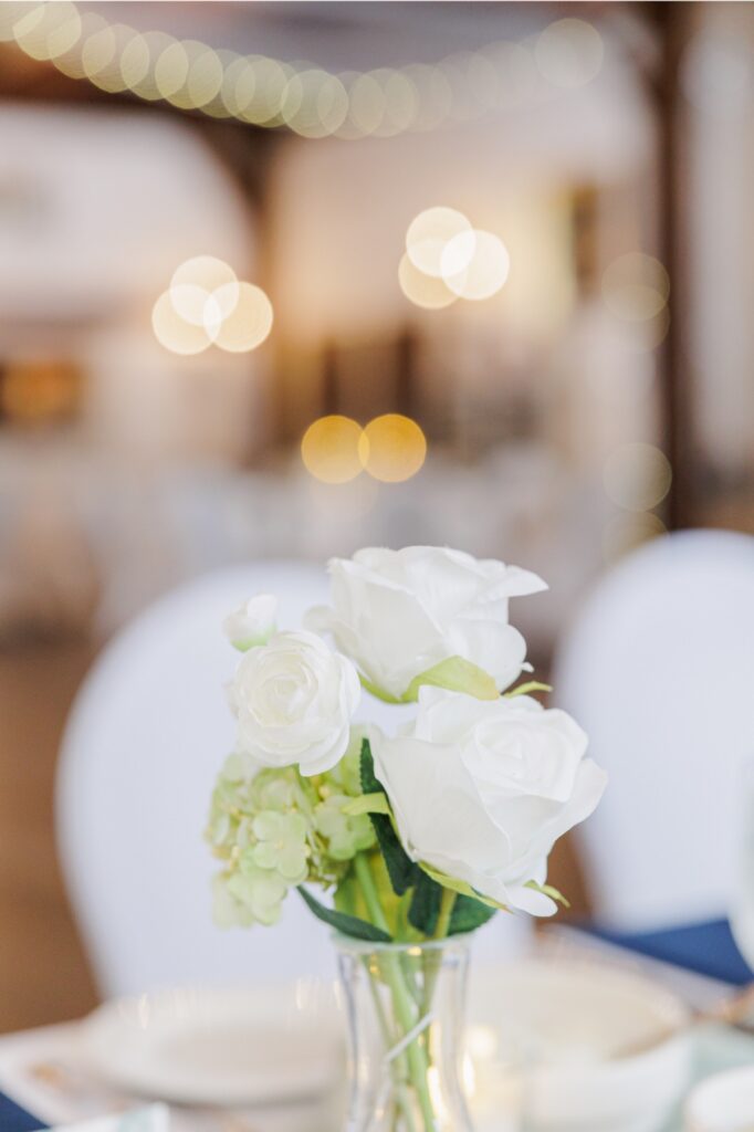 White rose centerpiece beneath warm lights in Paige Hall at the Publick House.