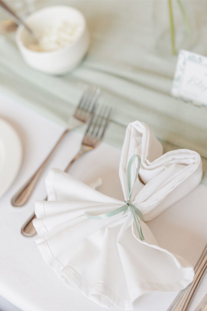 Napkin folded into a heart with a sage green ribbon at the wedding reception.