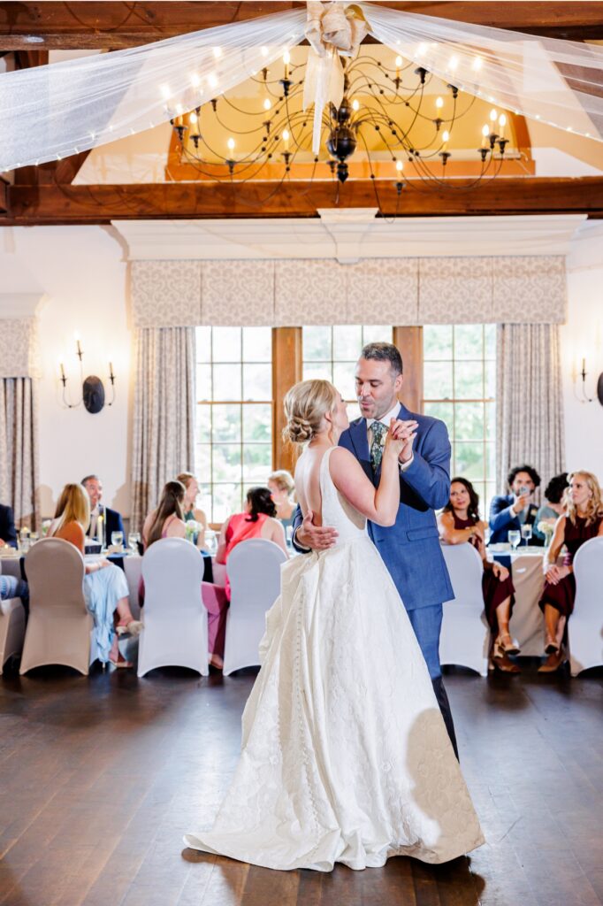 Bride and groom dance beneath chandeliers and exposed beams in Paige Hall.