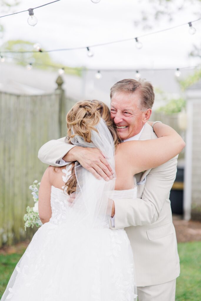 Father of the bride embraces his daughter during an emotional first look before the wedding ceremony. The bride’s veil and floral bouquet add to the intimate moment shared before the celebration.