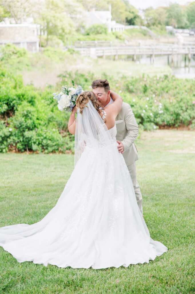 The bride and groom embrace during their first look on the waterfront lawn overlooking Wychmere Harbor. Their first hug captures the excitement of seeing one another before the wedding ceremony.