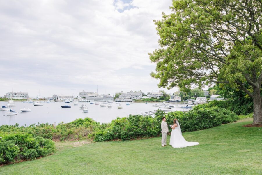 The bride and groom exchange private vows on a waterfront lawn overlooking Wychmere Harbor during their Wychmere Beach Club wedding. Sailboats and the Cape Cod shoreline create a peaceful backdrop for the intimate moment.