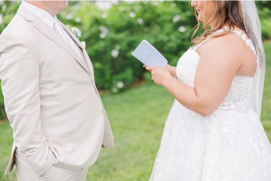 The bride reads her handwritten vows from a blue notebook while standing across from the groom during their private first look. The quiet exchange captures one of the most personal moments of their Cape Cod wedding.