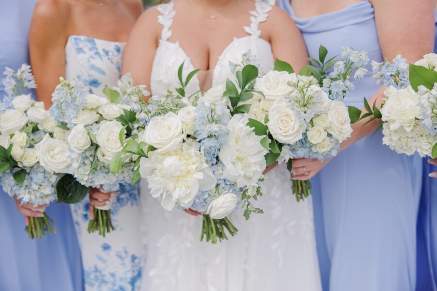 White roses, hydrangeas, ranunculus, pale blue delphinium, and fresh greenery fill the bridal bouquets held by the bride and bridesmaids. The soft blue and white florals suit the elegant coastal style of the Wychmere Beach Club wedding.