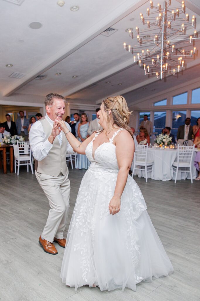 The bride dances with a family member while guests smile and watch from around the reception room at Wychmere. The lively moment captures the joy of celebrating together at their Cape Cod wedding.
