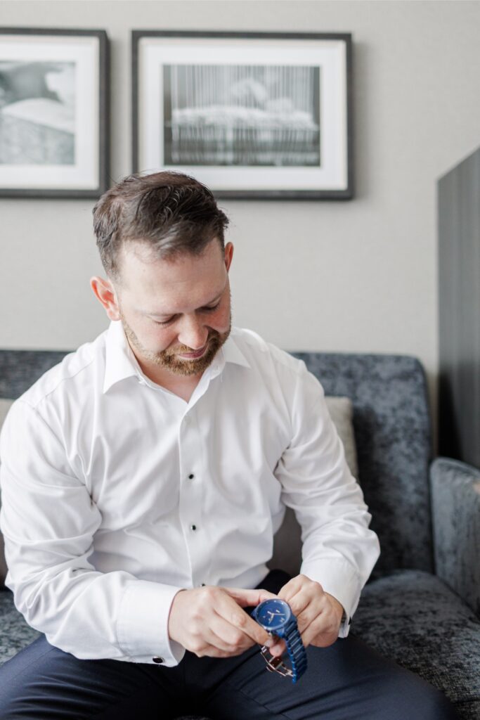 The groom looks down while getting ready in his Artisan Hotel room.