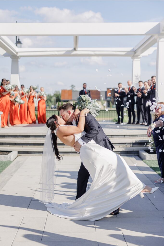 The groom dips the bride for a kiss as guests celebrate at the end of their outdoor ceremony.