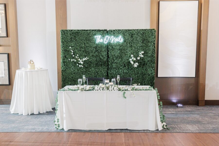 Artisan Hotel wedding sweetheart table set against a greenery wall with a white neon sign.