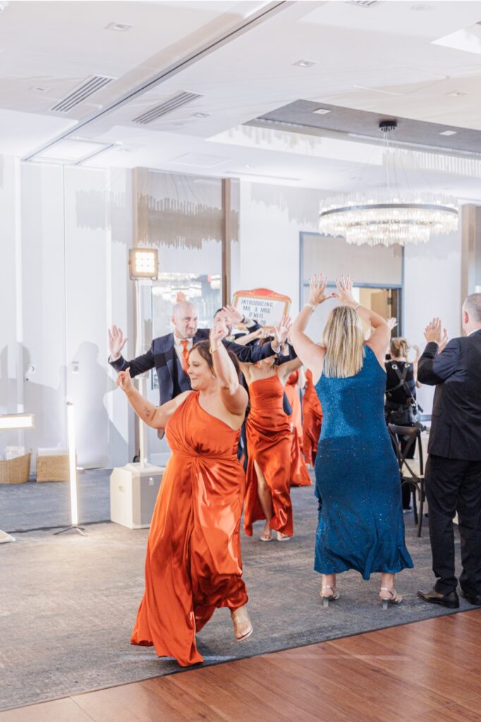 Bridesmaids in burnt orange dresses dance into the Artisan Hotel ballroom.