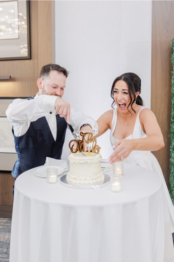 The bride and groom laugh while cutting their wedding cake.