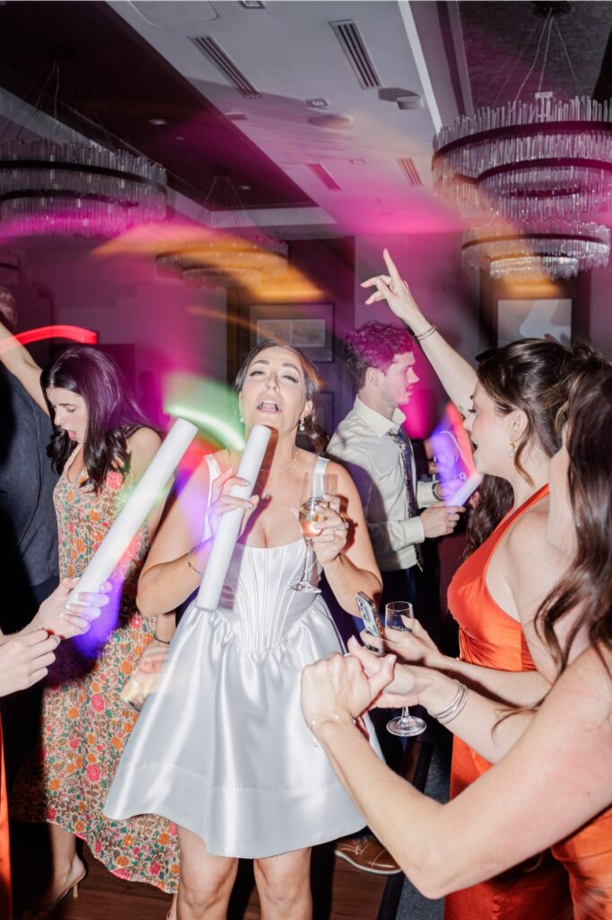 The bride celebrates with friends and colorful glow sticks on the packed dance floor.