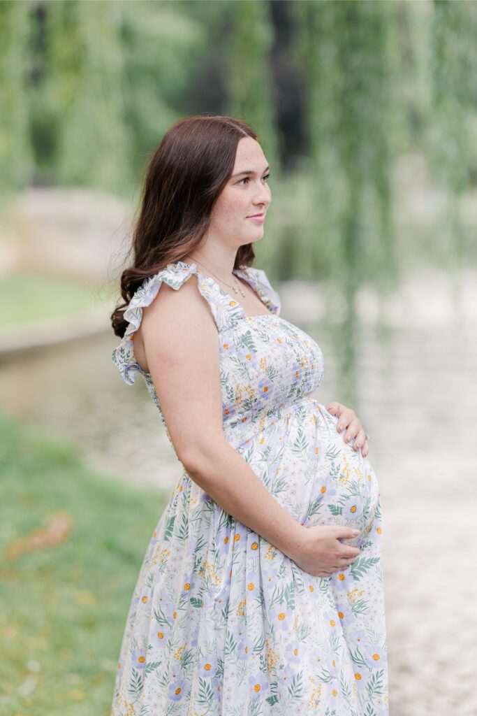 A pregnant mom holding her belly and looking out at the lagoon at the Boston Public Garden during her maternity photos.