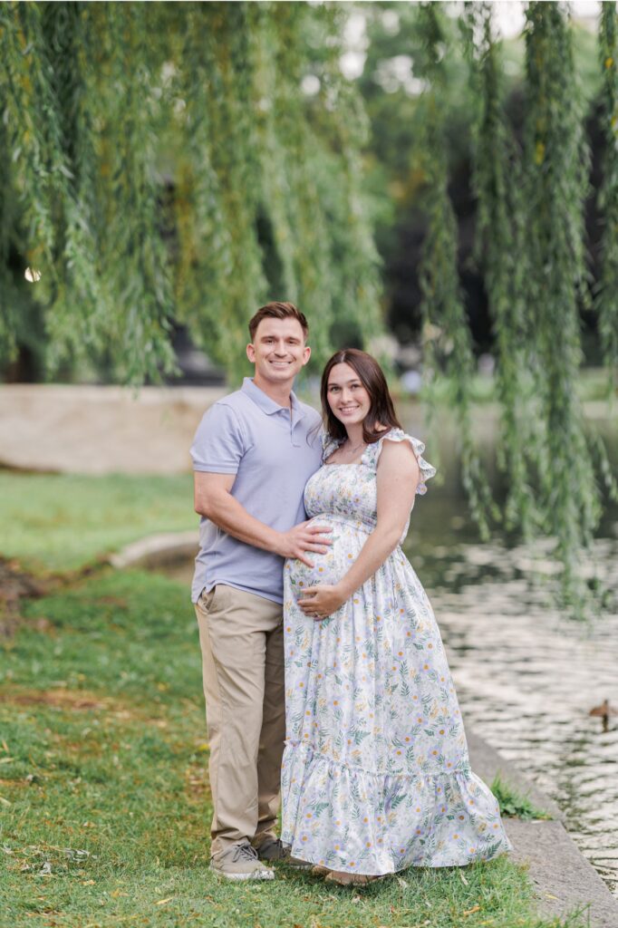 A portrait of expecting parents looking at the camera and smiling during their Boston Public Garden maternity pictures