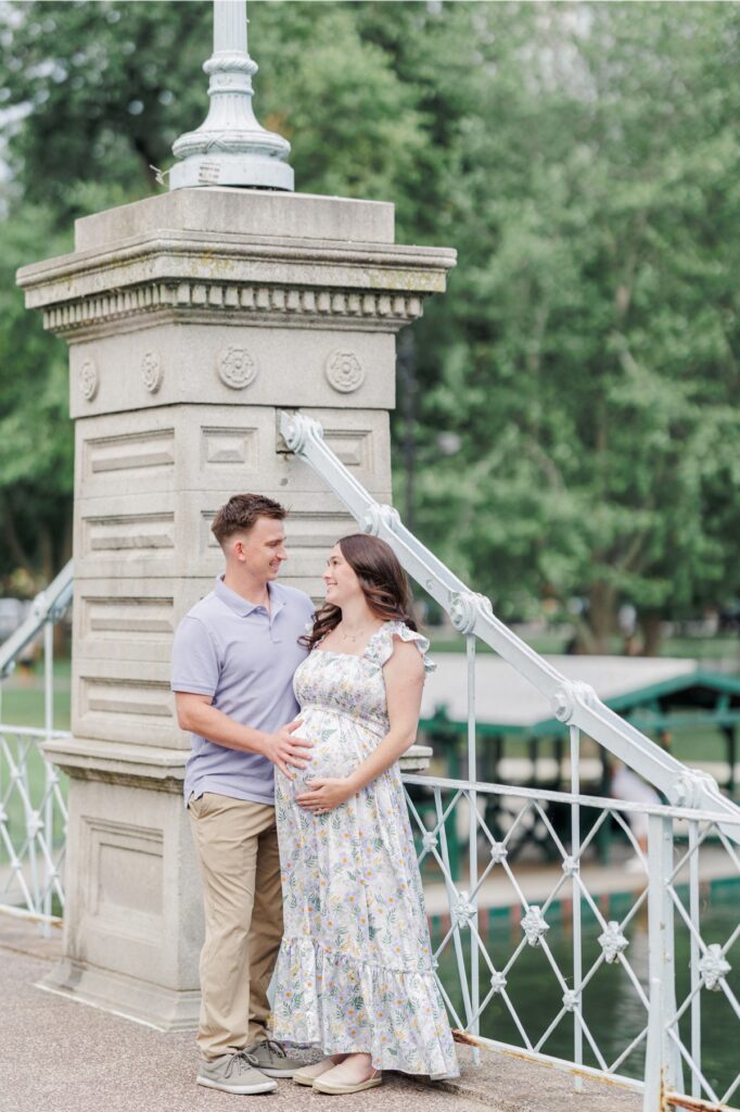 A man holding the stomach of his pregnant wife's belly on the bridge at the Boston Public Garden