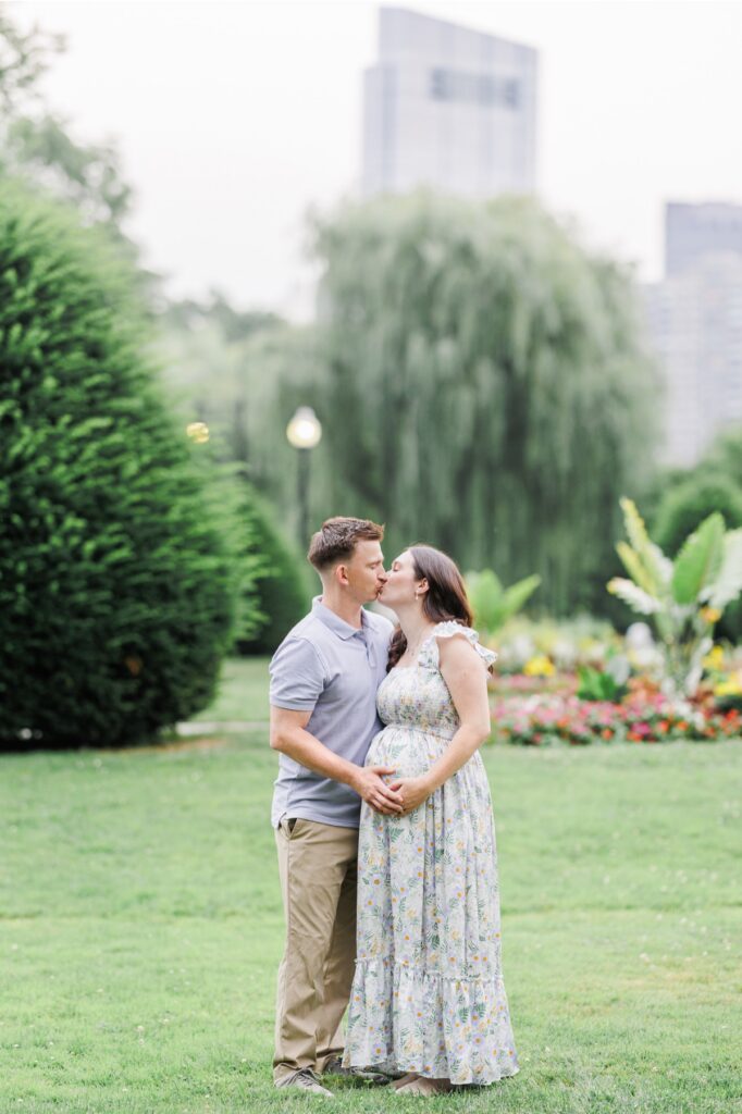 A man and woman kissing while they hold on to the woman's pregnant belly during their Boston Public Garden maternity session.