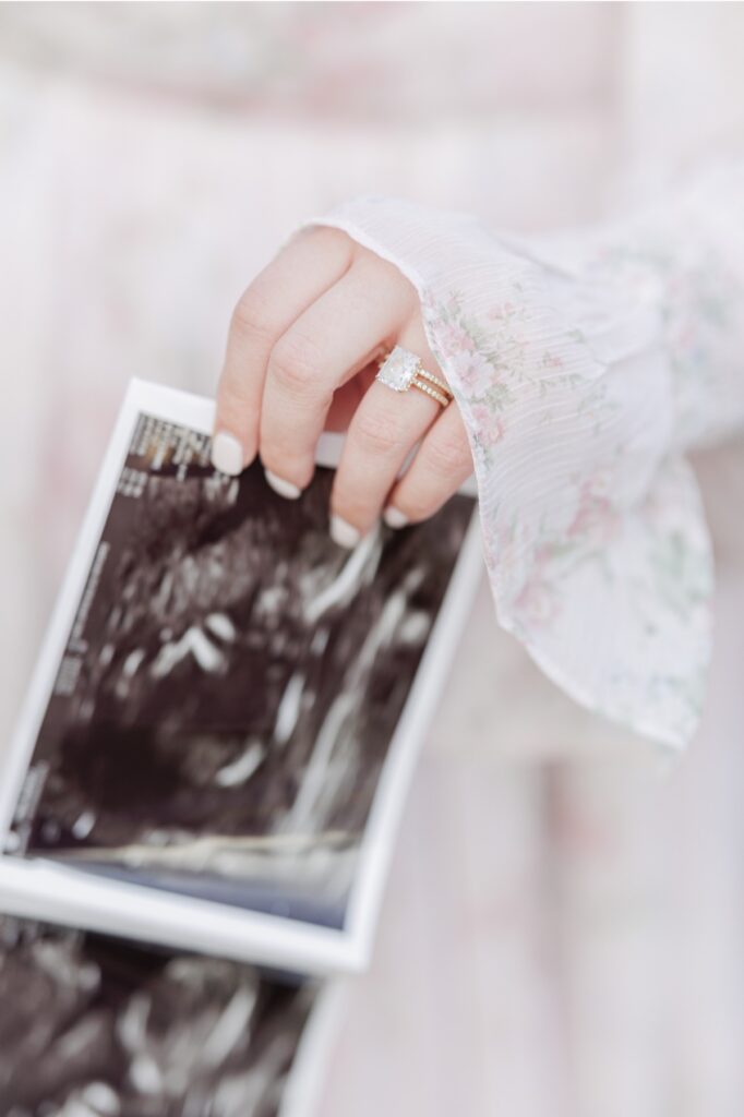 A close up of a woman's hand holding sonogram photos in front of a flowy pink dress.