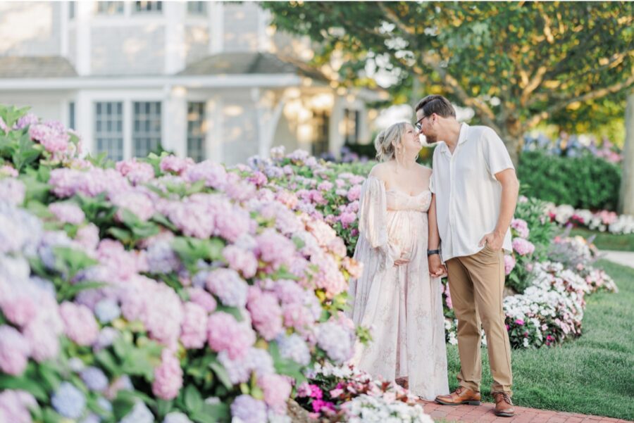 A couple holding hands and smiling at each other next to hydrangea flowers at Chatham Bars Inn during their maternity photos.