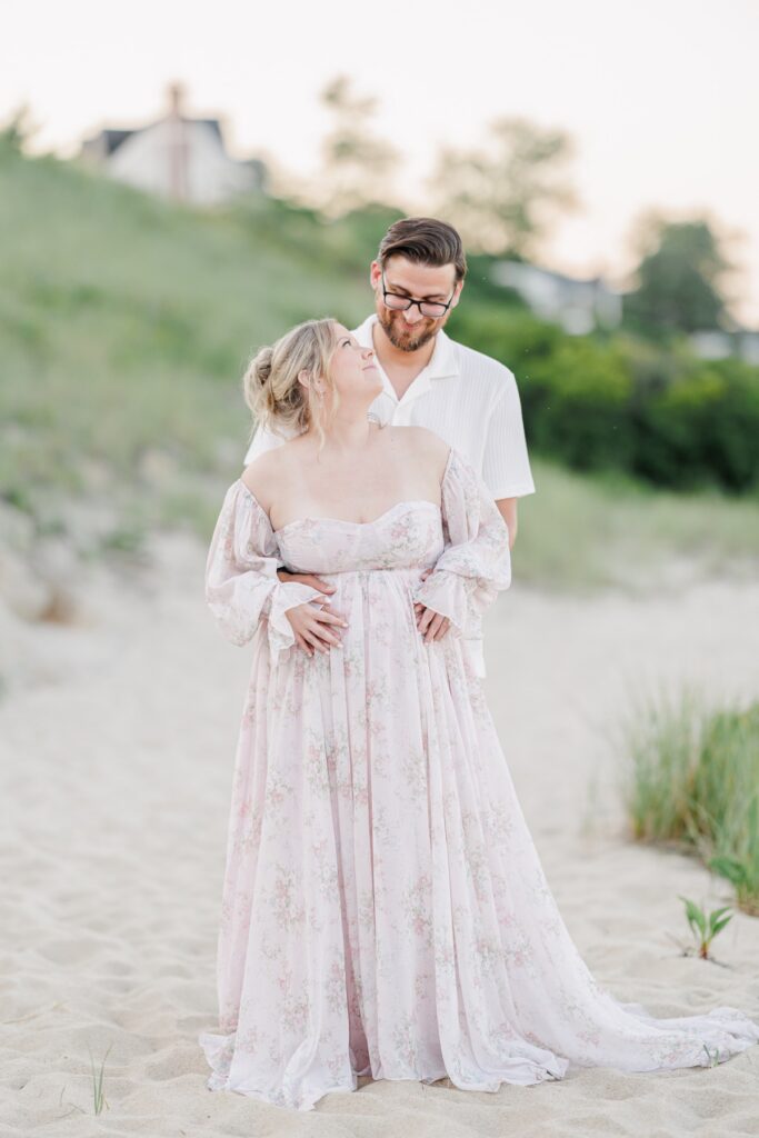 A couple hugging as the pregnant woman looks up and smiles and the man on Chatham Light beach during their maternity photos