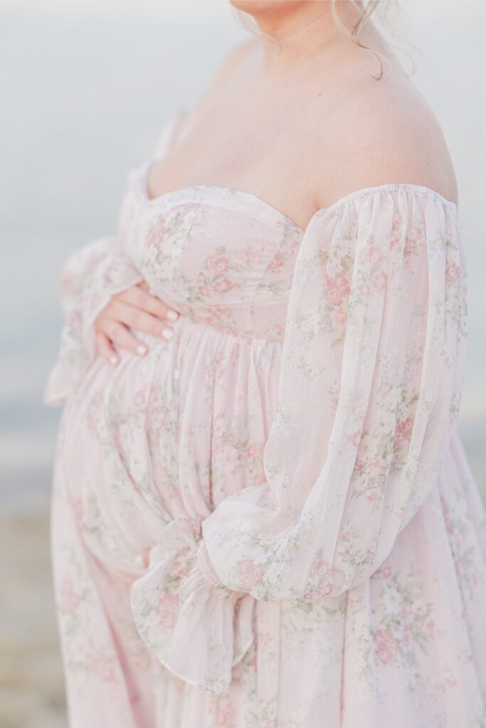 A close up of a pregnant woman holding her belly during her maternity photos at Chatham Lighthouse Beach