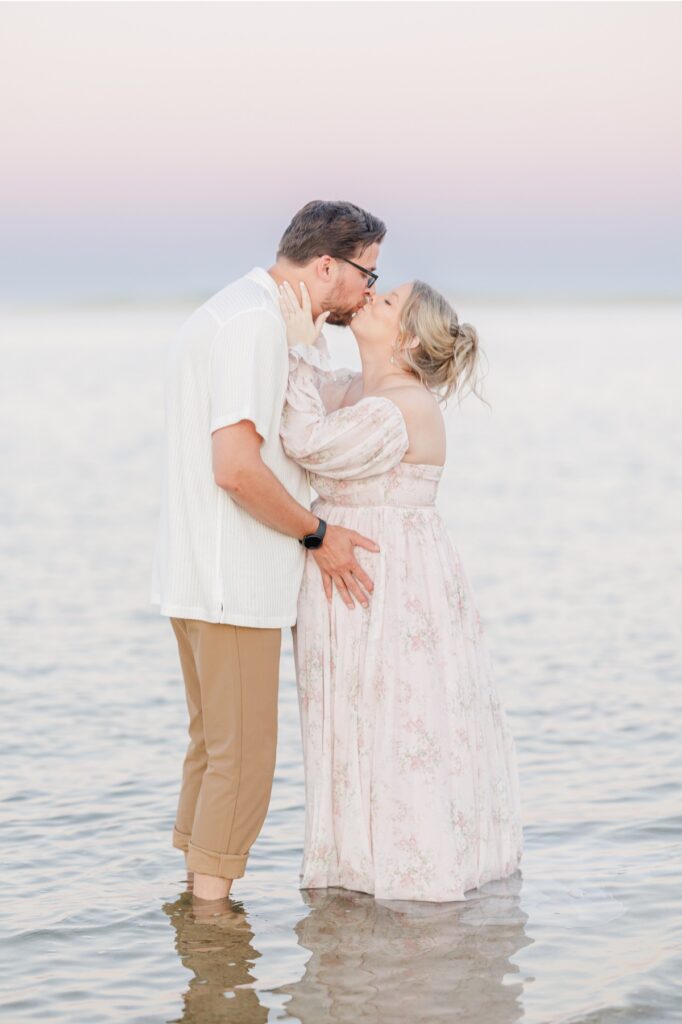 A couple standing in the ocean and kissing during their Chatham Lighthouse Beach maternity pictures