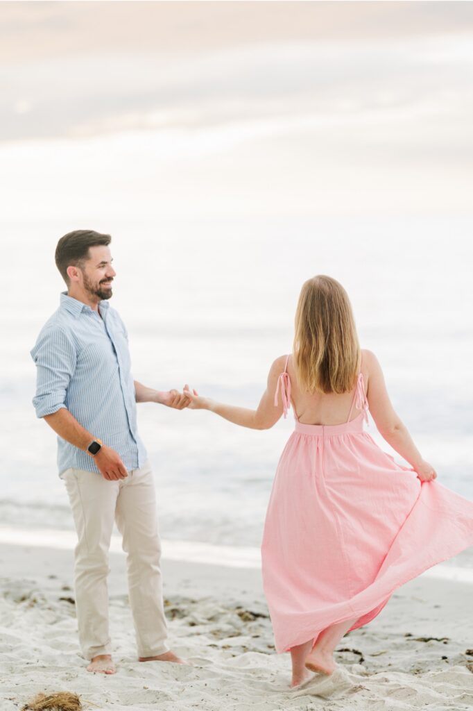 Amy twirls her pink dress while holding Joe's hand during their Mayflower Beach engagement photos.