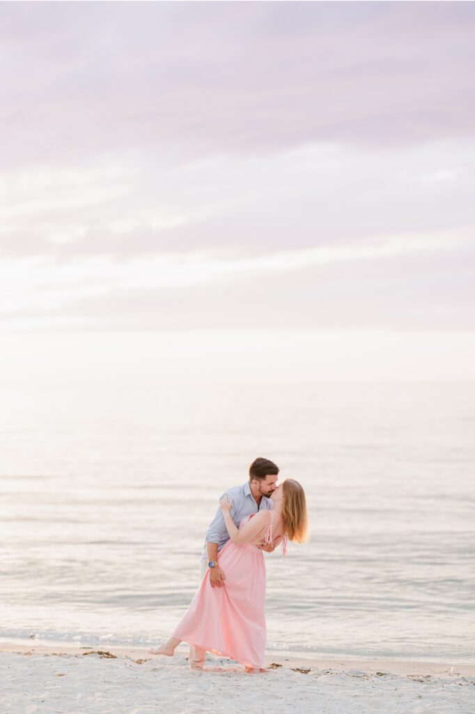 Joe dips and kisses Amy beneath the pastel evening sky at Mayflower Beach.