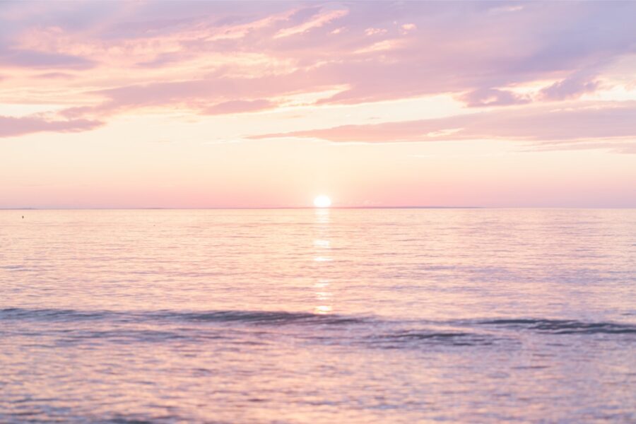 A pink and lavender summer sunset glows over the water at Mayflower Beach in Dennis, Massachusetts.