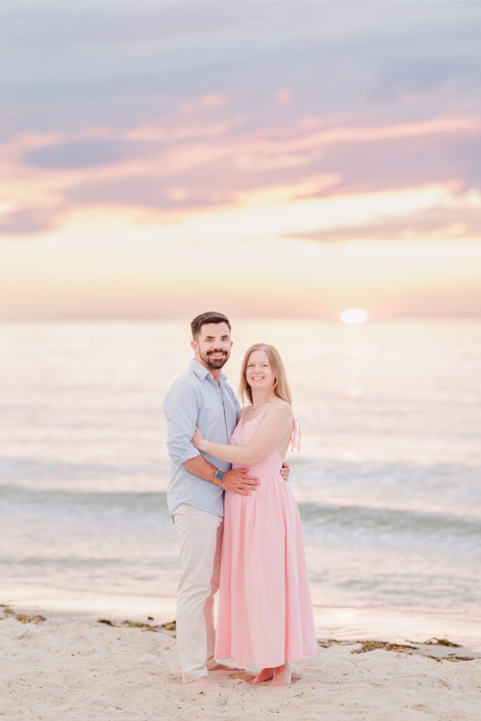  Amy and Joe embrace beneath a vivid pink sunset at Mayflower Beach on Cape Cod.