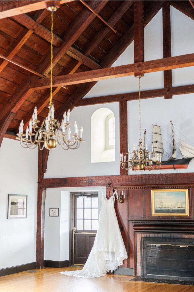 Lace bridal gown hanging beneath wood beams, brass chandeliers, and a model ship at Salem Country Club.