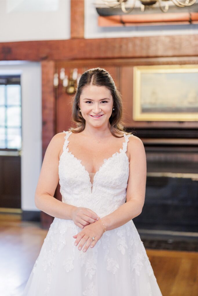 The bride smiling in her lace gown in front of the fireplace at her Salem Country Club wedding.