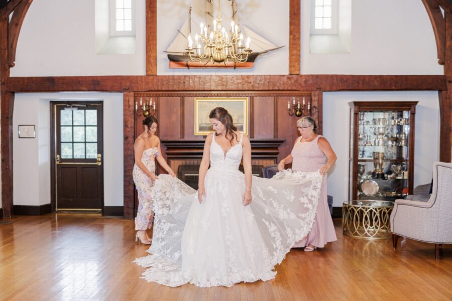 Two women arranging the bride’s lace train in the nautical room before her Salem Country Club wedding.