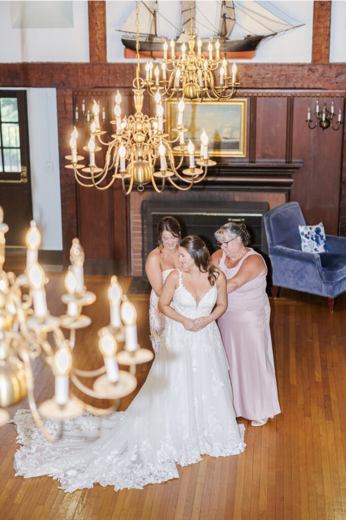 The bride receiving help with her gown beneath brass chandeliers before her Salem Country Club wedding.
