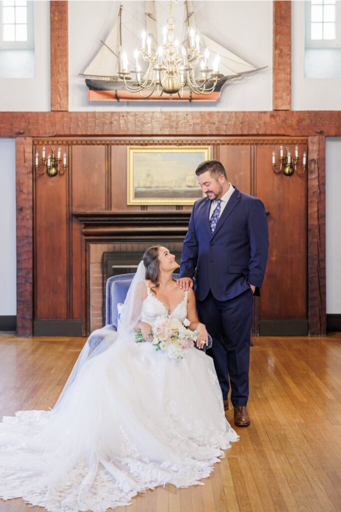 The groom resting a hand on the seated bride’s shoulder during their Salem Country Club wedding portraits.