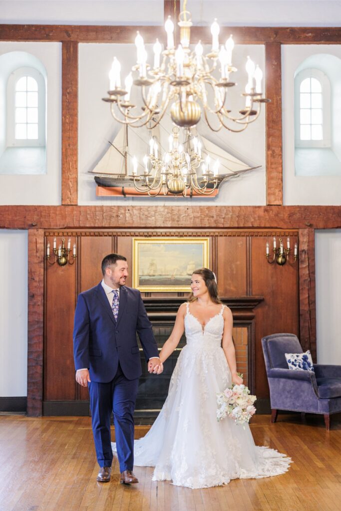 The bride and groom holding hands beneath a model sailing ship at their Salem Country Club wedding.
