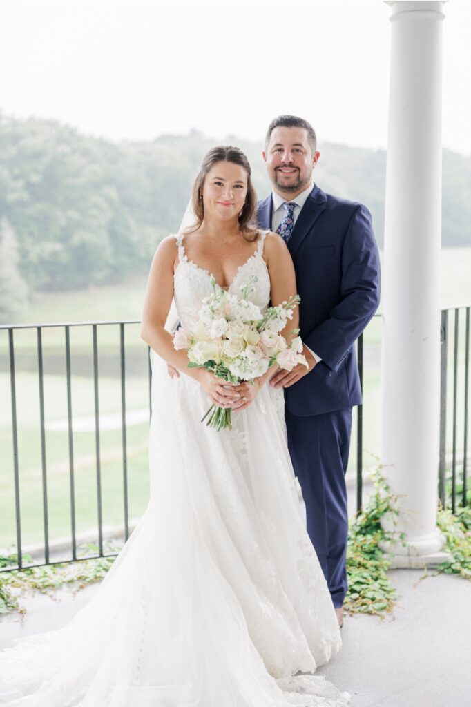 The bride holding her blush and white bouquet with the groom behind her during Salem Country Club wedding portraits.