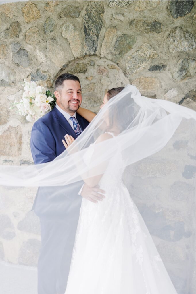 The groom smiling as the bride’s long veil sweeps around them during Salem Country Club wedding portraits.