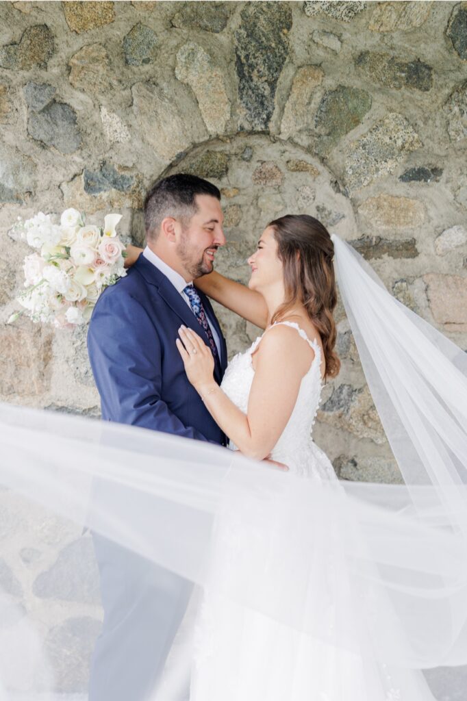 The bride and groom smiling at each other beside a stone wall during Salem Country Club wedding portraits.