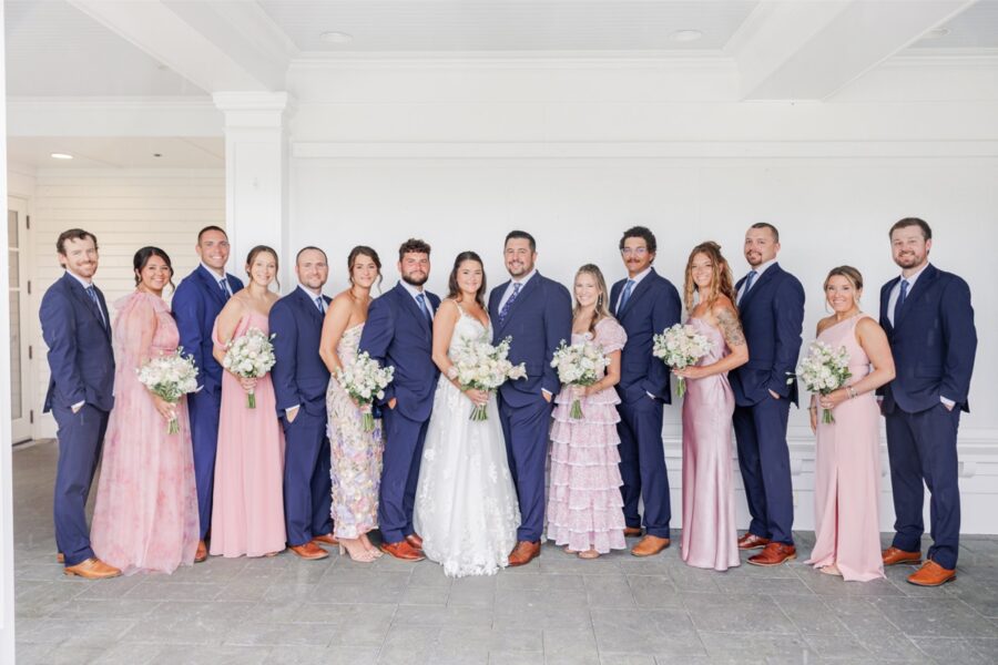 The bride and groom with their wedding party in navy suits and pink dresses on the Salem Country Club covered porch.